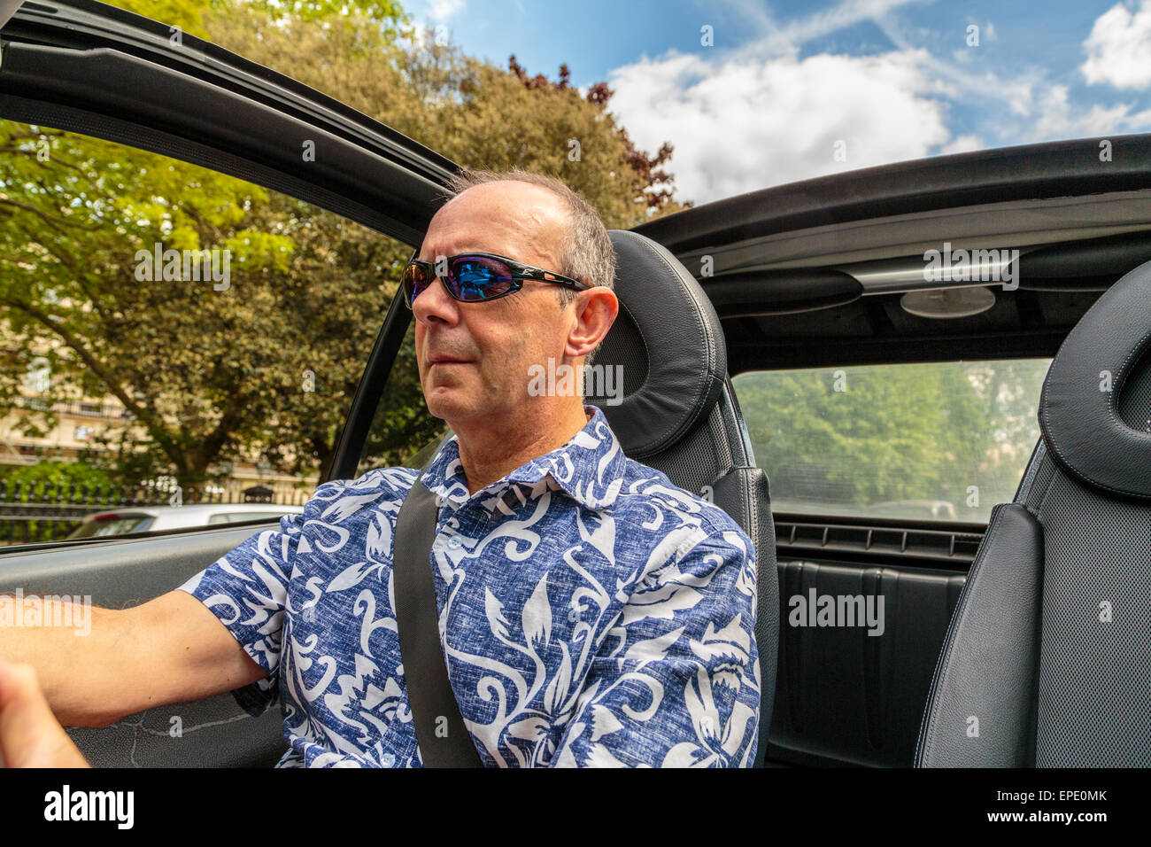 Un hombre de mediana edad conducir un coche Cabriolet con el techo hacia abajo en un día de verano en Londres England Reino Unido Foto de stock