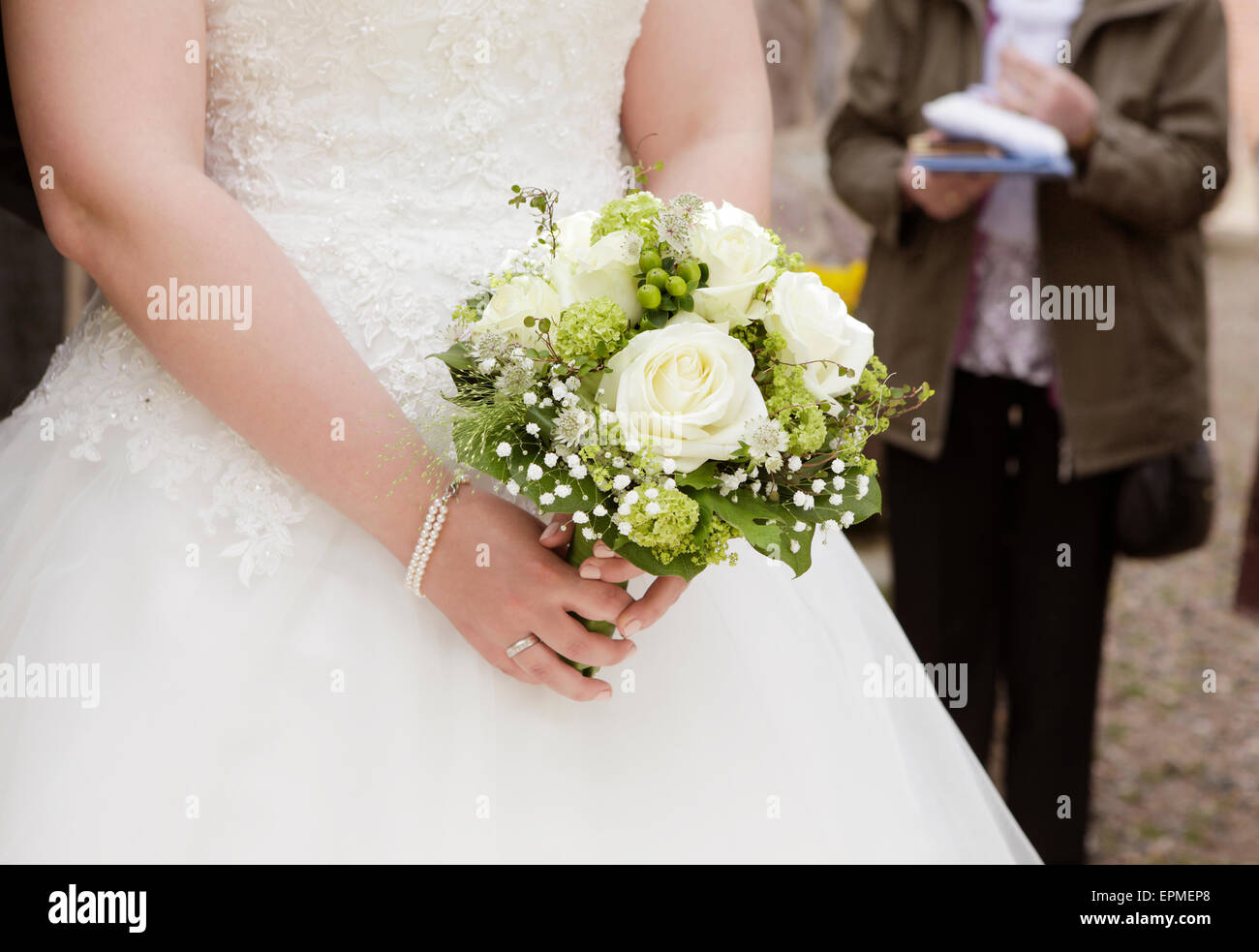 Una novia en un vestido blanco sosteniendo un ramo de novia con rosas en la mano Foto de stock