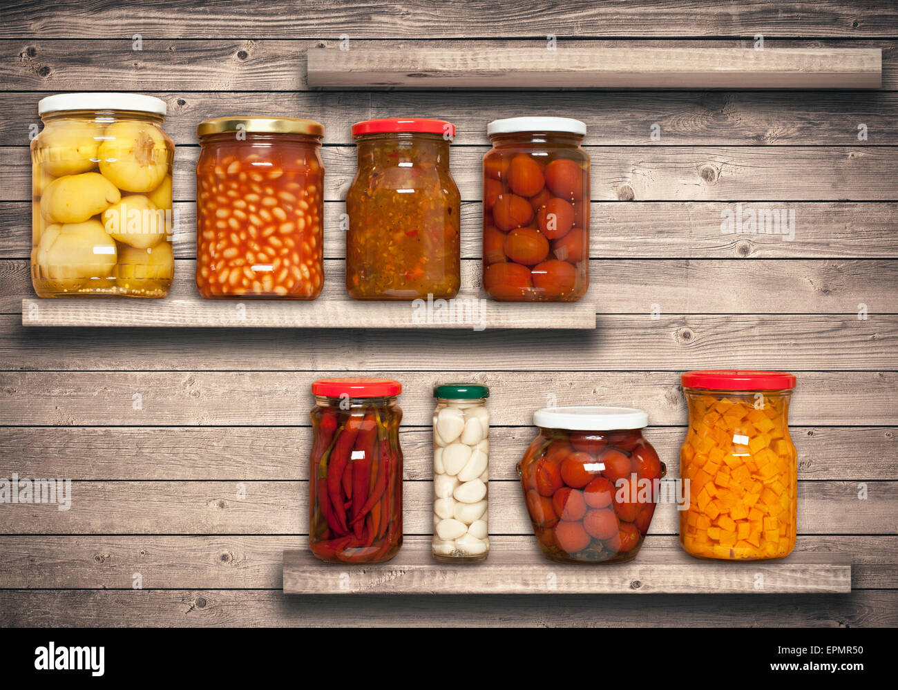 Conserva las zanahorias, tomates, ajo, chile, frijoles en la estantería cerca de una pared de madera marrón Foto de stock