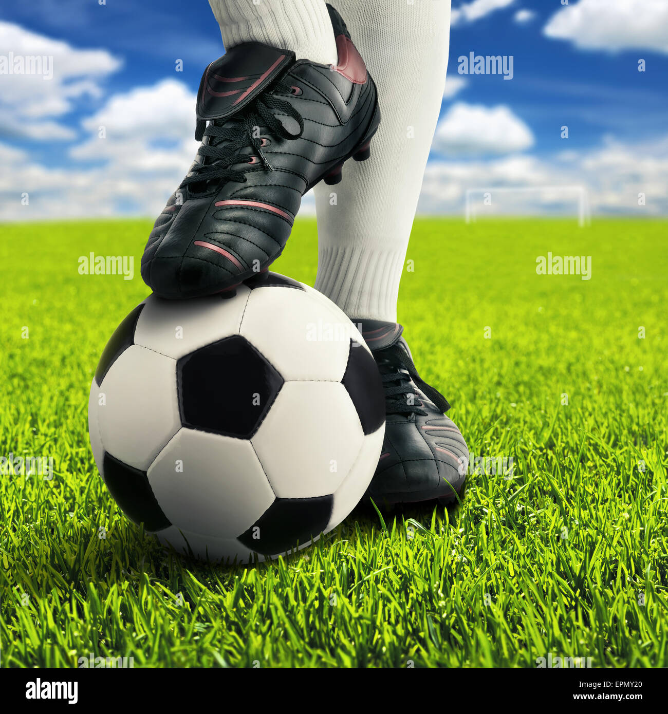 Los pies del jugador de fútbol en pose casual en un campo de juego abierto, con el cielo de fondo Foto de stock