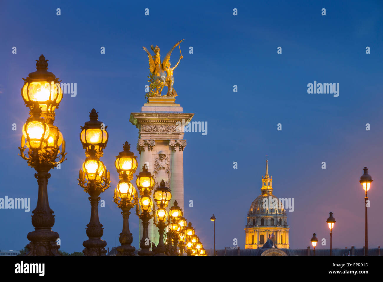 Fila de farolas a lo largo Puente Alexandre III con cúpula del Hotel des Invalides más allá, París, Francia Foto de stock