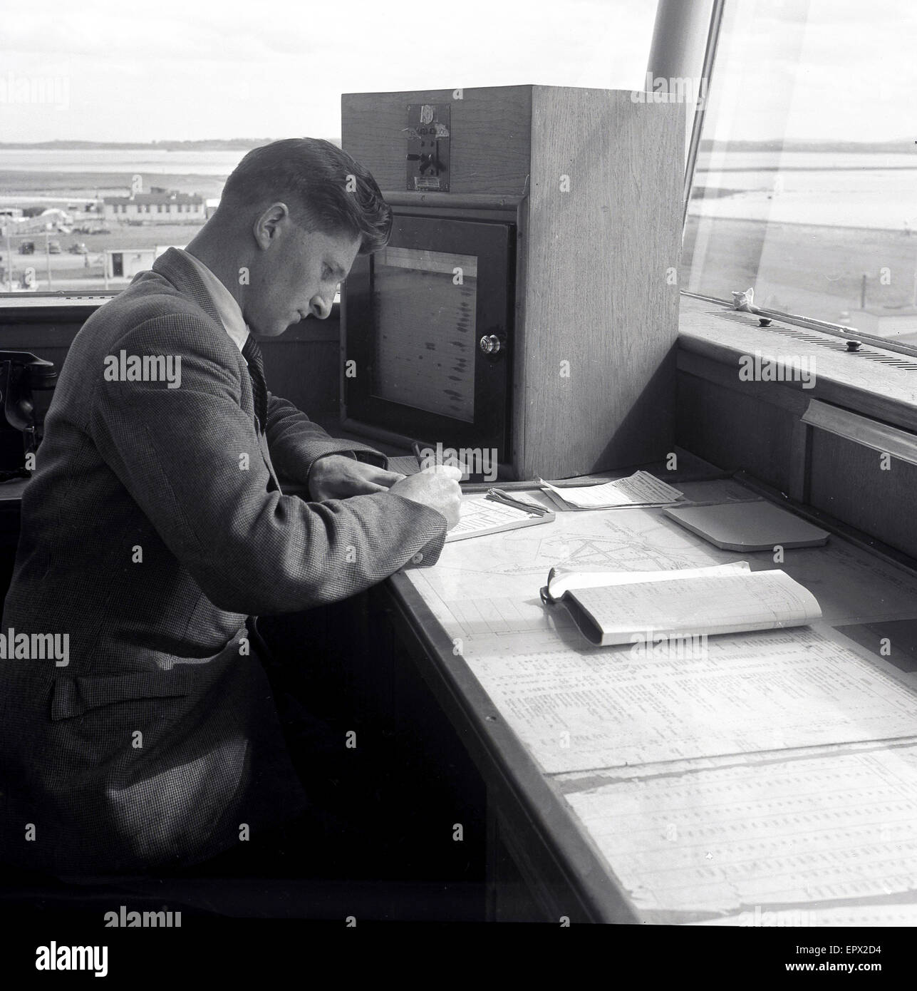 1950, histórico, un controlador de tráfico aéreo macho en una mesa de trabajo en la torre de control del aeropuerto por la pista de aterrizaje, el aeropuerto de Dublín, Irlanda. Foto de stock