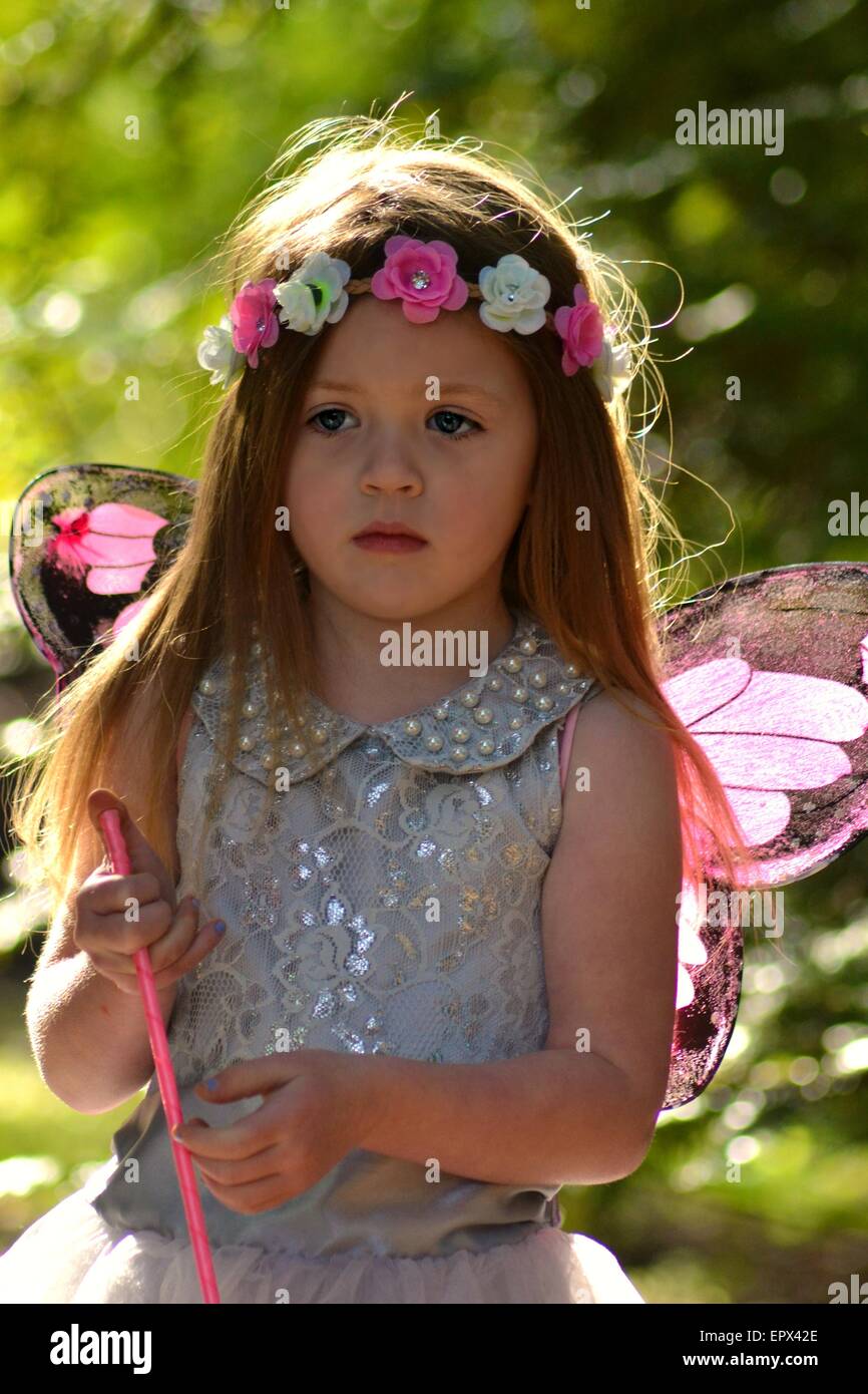 Joven rubia chica con bonitos ojos azules con una diadema de flor rosa y blanco y rosa y negro alas de hadas. Foto de stock