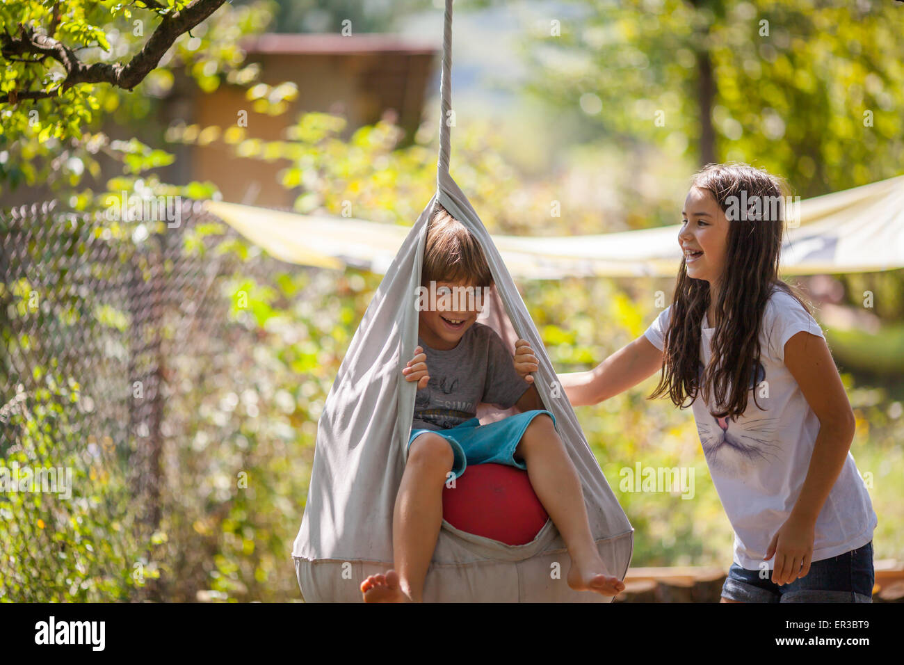 Niño y niña jugando en un columpio en el jardín Foto de stock