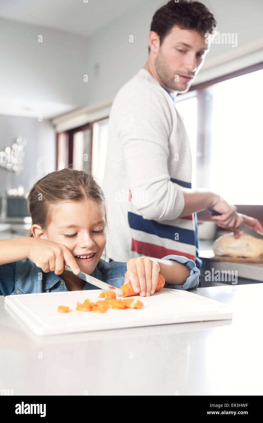 Niña ayudando a su padre a preparar la comida en la cocina Foto de stock