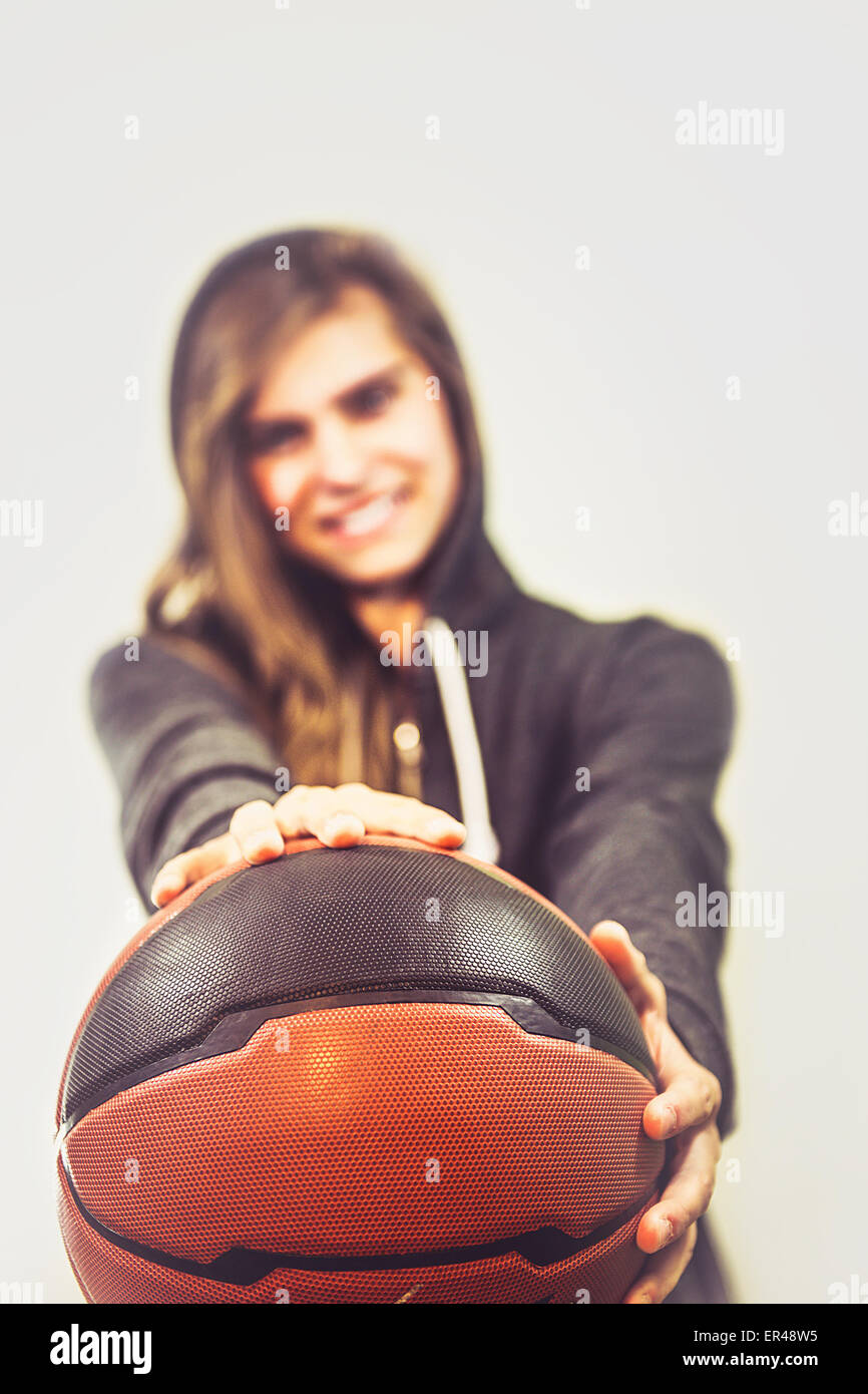 Niña está sosteniendo una pelota de baloncesto y sonriente. Ella llevaba una chaqueta con capucha de deportes. Niza, los colores cálidos de la foto. Foto de stock