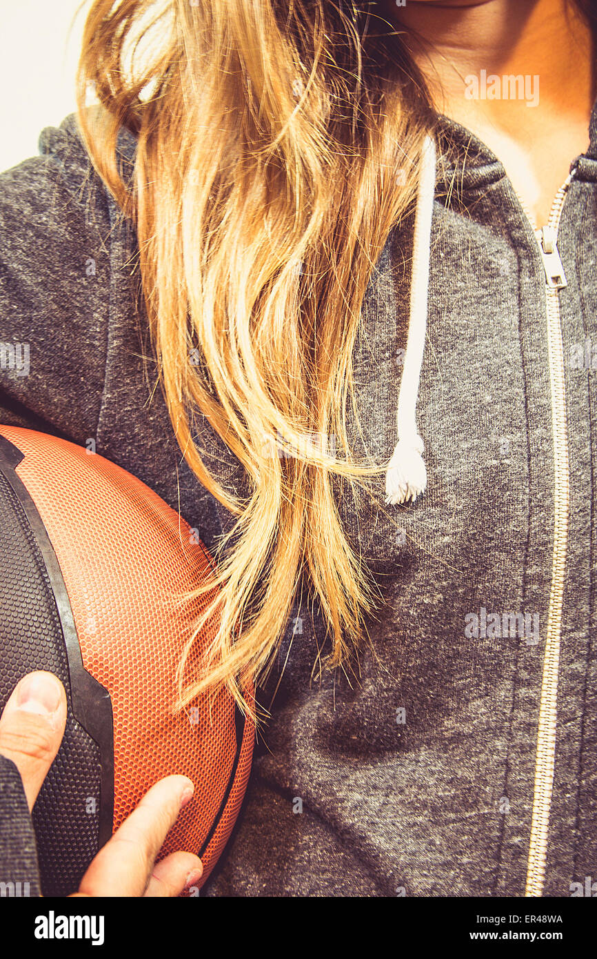 Niña está sosteniendo una pelota de baloncesto y sonriente. Ella llevaba una chaqueta con capucha de deportes. Niza, los colores cálidos de la foto. Foto de stock