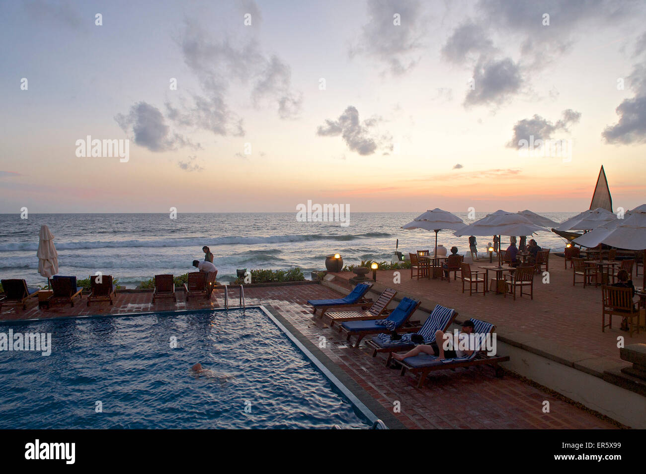 Personas alrededor de la piscina con vistas al mar al atardecer en el Galle Face Hotel, Colombo, Sri Lanka Foto de stock