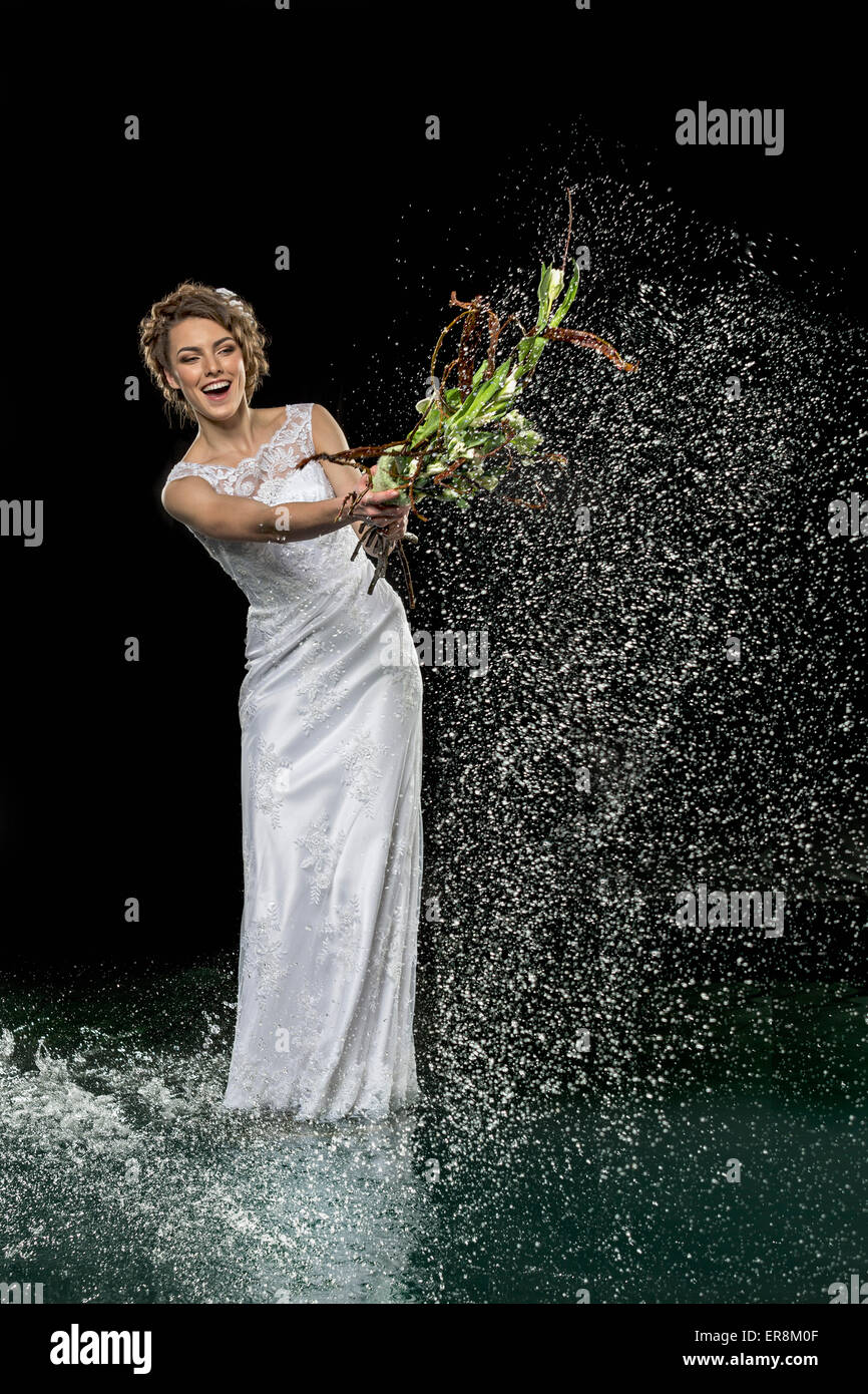 Emocionada joven novia ramo contra salpicaduras de agua con fondo negro Foto de stock