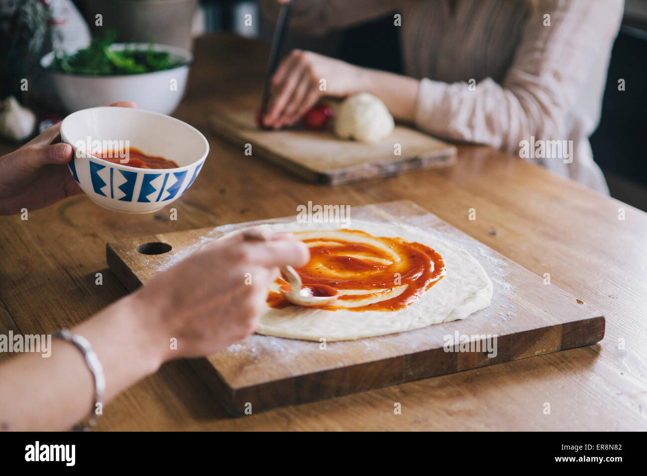 Imagen recortada de la mujer extiende la salsa de tomate sobre la masa de pizza Foto de stock