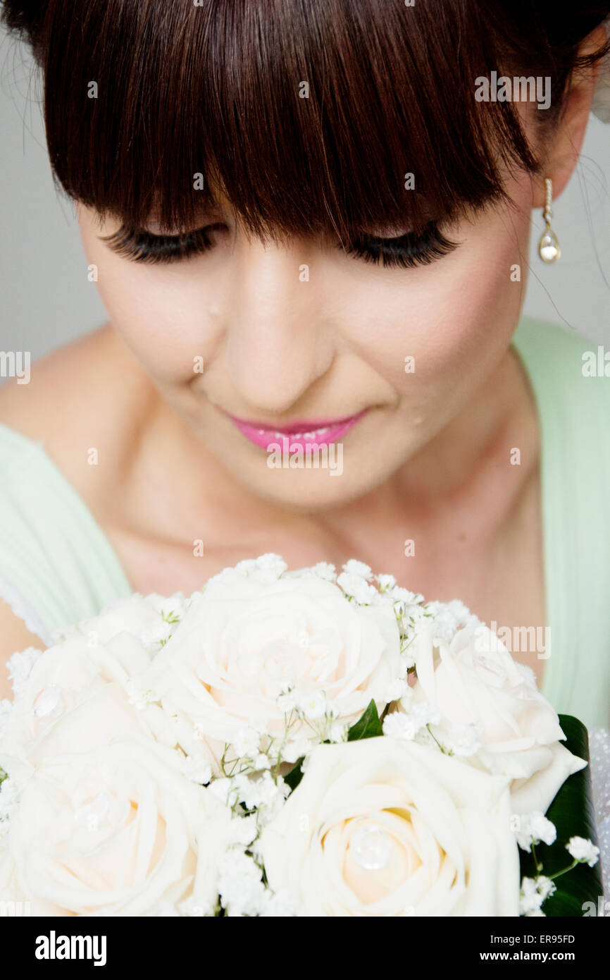 Novia posando después de conseguir maquillaje profesional para el día de su boda, hermoso rostro y bouquet closeup.Novia tiene flequillo. Foto de stock