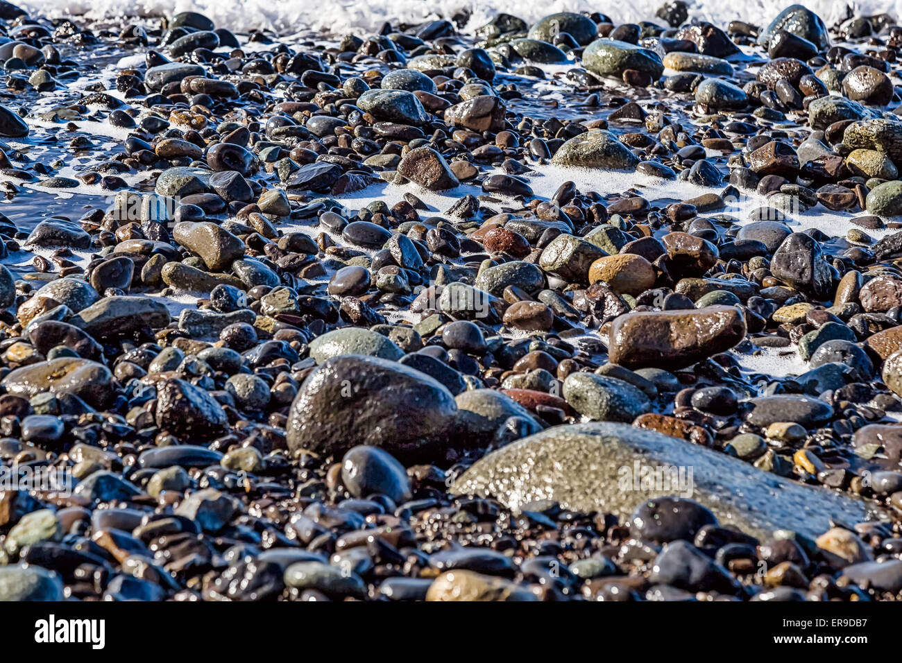 Piedras con espuma en la orilla de la playa del océano o mar Foto de stock
