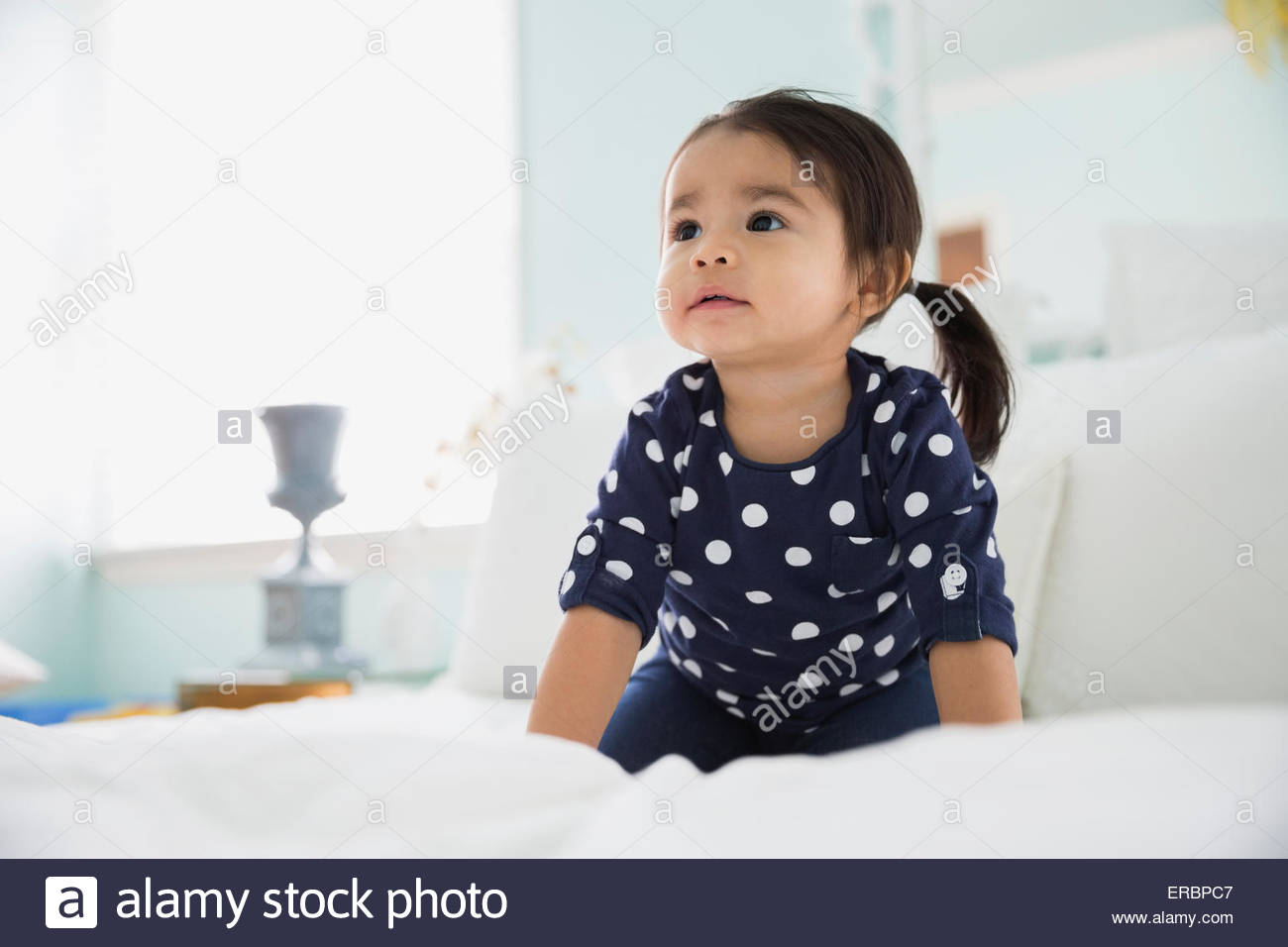 Curiosa niña morena, mirando hacia arriba en la cama Foto de stock