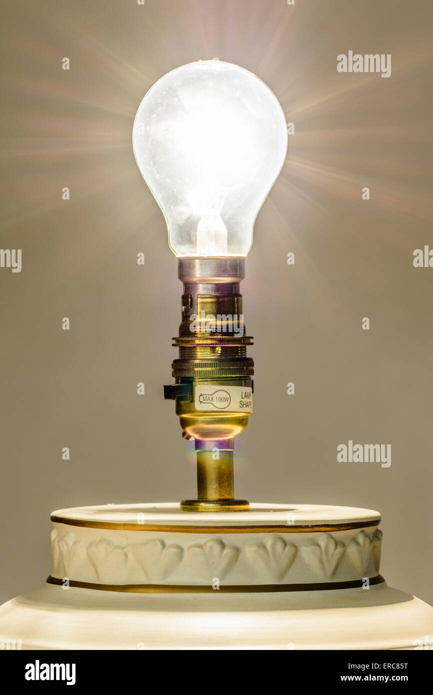 Antiguo tipo de bombilla eléctrica incandescente en una lámpara encendida, con rayos de luz emanando. Foto de stock
