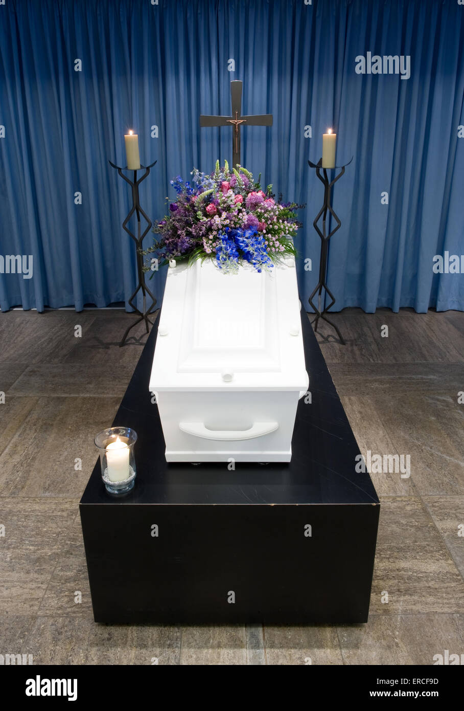 Un ataúd con un arreglo de flores en una morgue con dos velas encendidas y una cruz Foto de stock