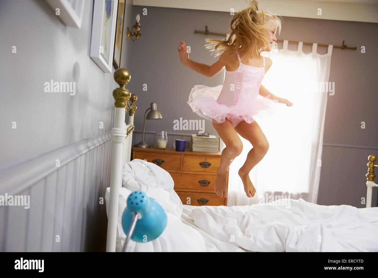Chica en traje de bailarina saltar en la cama de los padres. Foto de stock