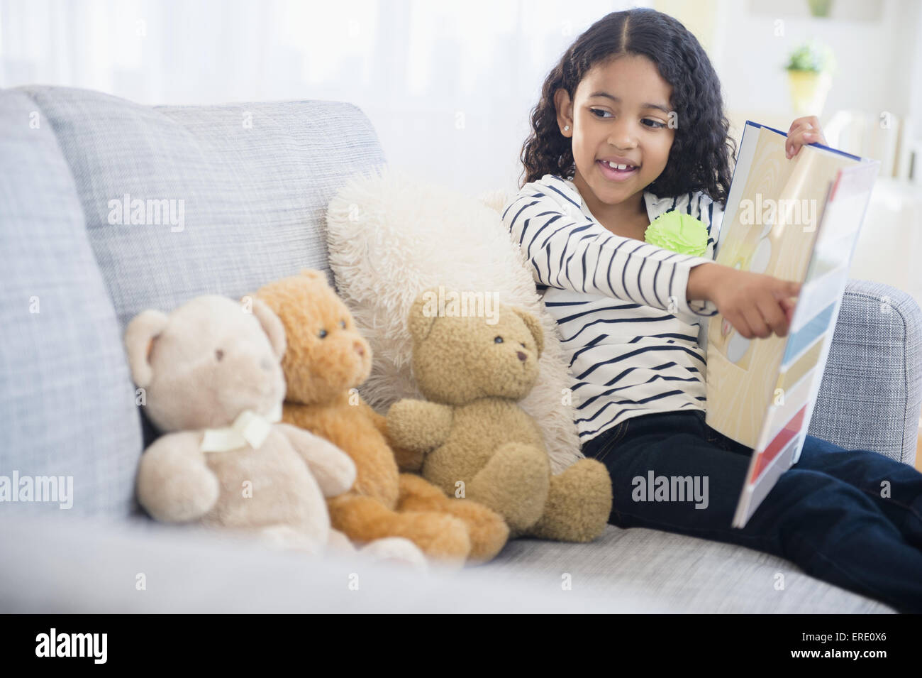 Raza mixta chica enseñando los osos de peluche en el sofá Foto de stock