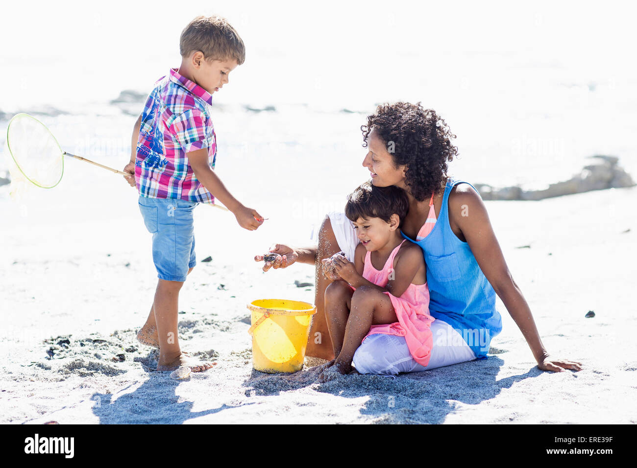 Madre de raza mixta y niños jugando en la playa Foto de stock