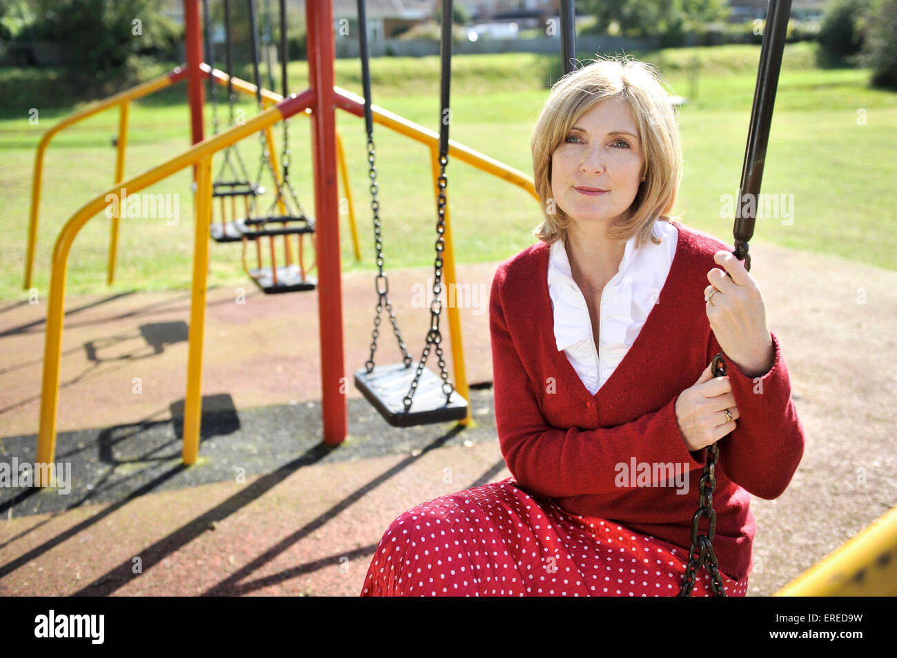 Una mujer en rojo se sentó en un columpio en un parque. Foto de stock