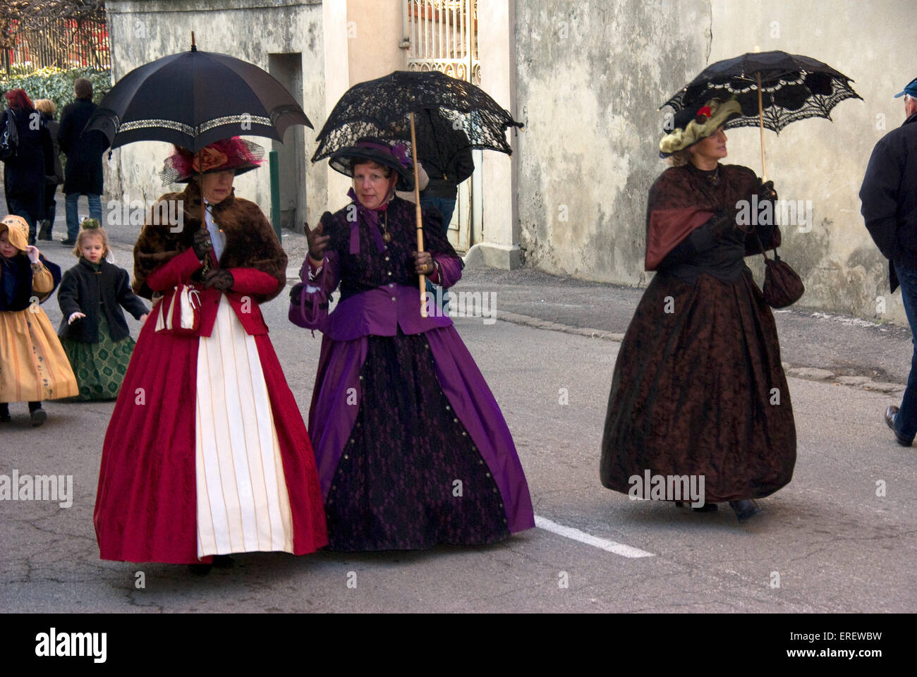 Tres damas en trajes de estilo Victoriano con sombrillas, tomando parte en un desfile del Día de San Valentín en la aldea de Roquemaure, Foto de stock