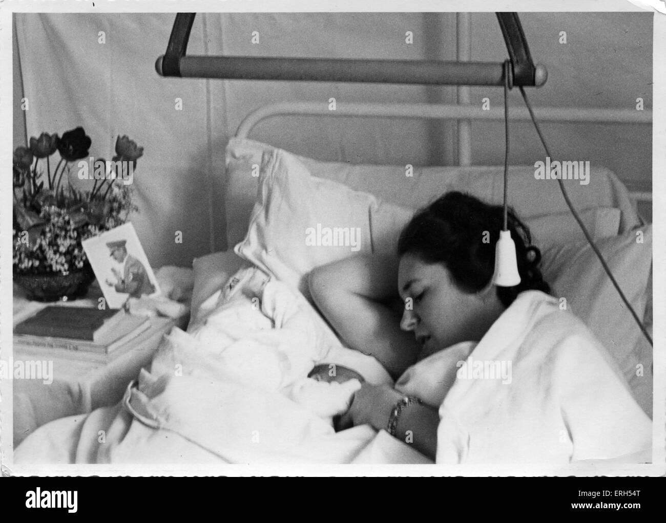 Una mujer con bebé recién nacido yace en su cama del hospital con un retrato de Hitler en la cabecera. Foto de stock