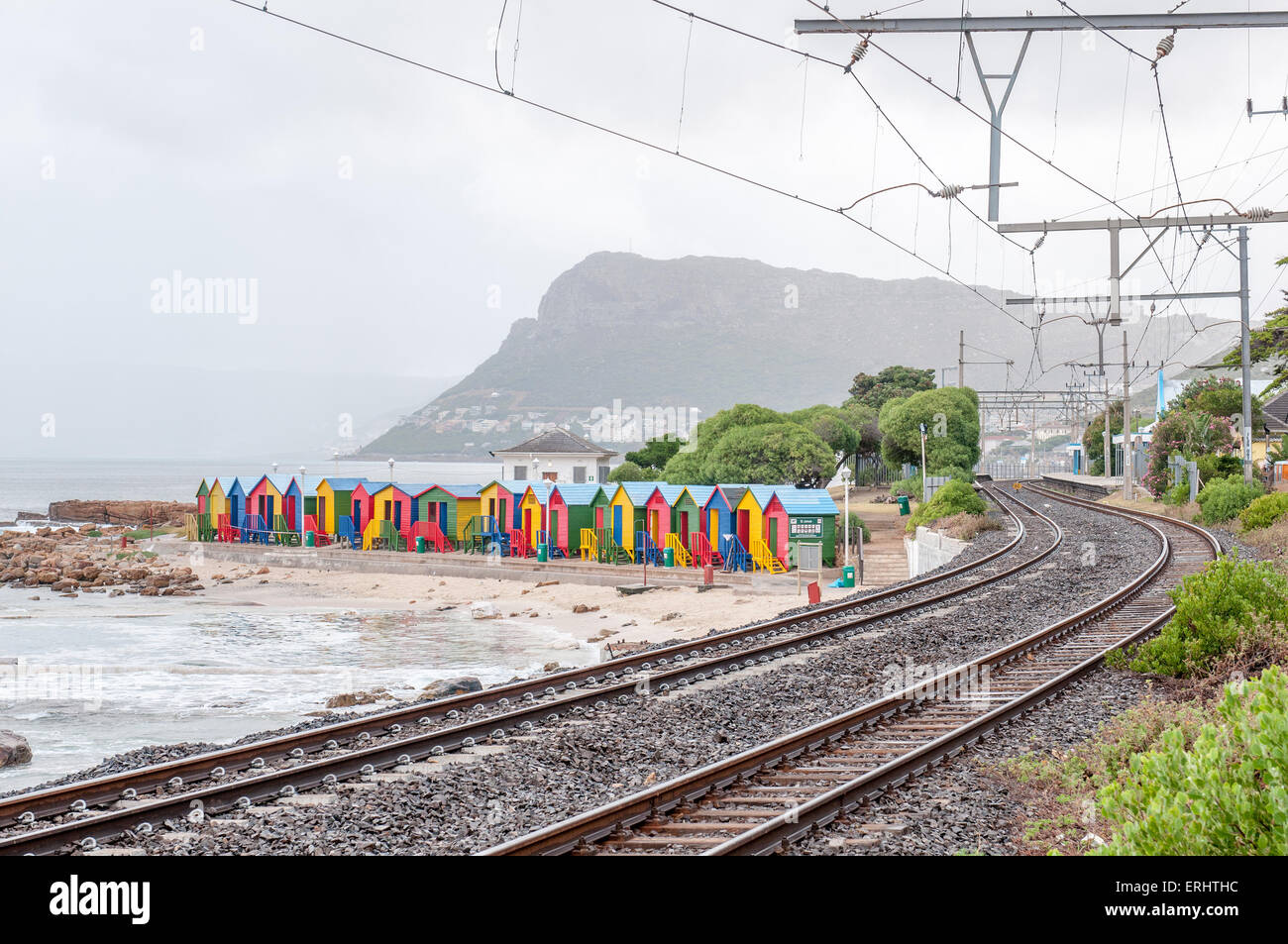 Multicolores de cabañas de playa en St. James en Cape Town, Provincia del Cabo Occidental de Sudáfrica. La estación de ferrocarril y es visible Foto de stock