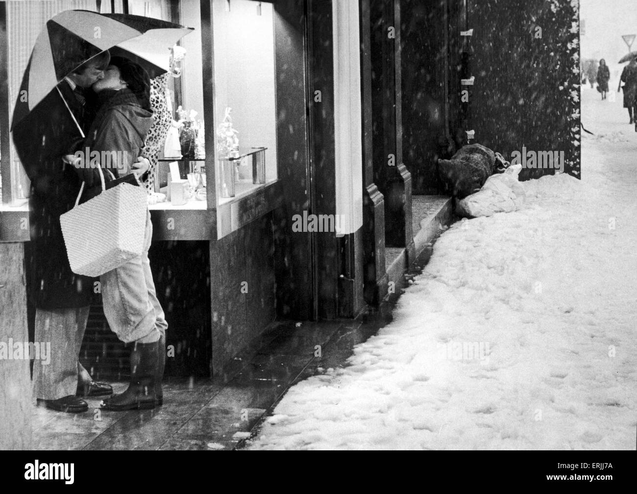 Ellos tienen su amor para mantenerlos calientes..Esta pareja joven encontrado el amor en brazos de los demás en una calle de Edimburgo, desapercibidos por los transeúntes luchando tirar la nieve y el aguanieve. Era el único momento de fusión en la ciudad de ayer. El 10 de enero de 1979 Foto de stock