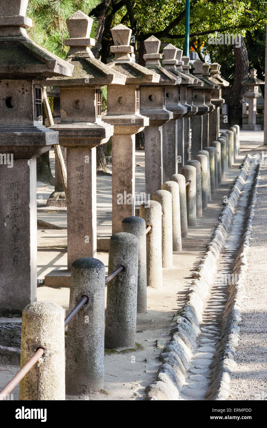Santuario de Nishinomiya Japón. Vea a lo largo de una línea de faroles de  piedra que langran sombras con pequeños pilares de piedra formando una  valla delante de ellos Fotografía de stock -