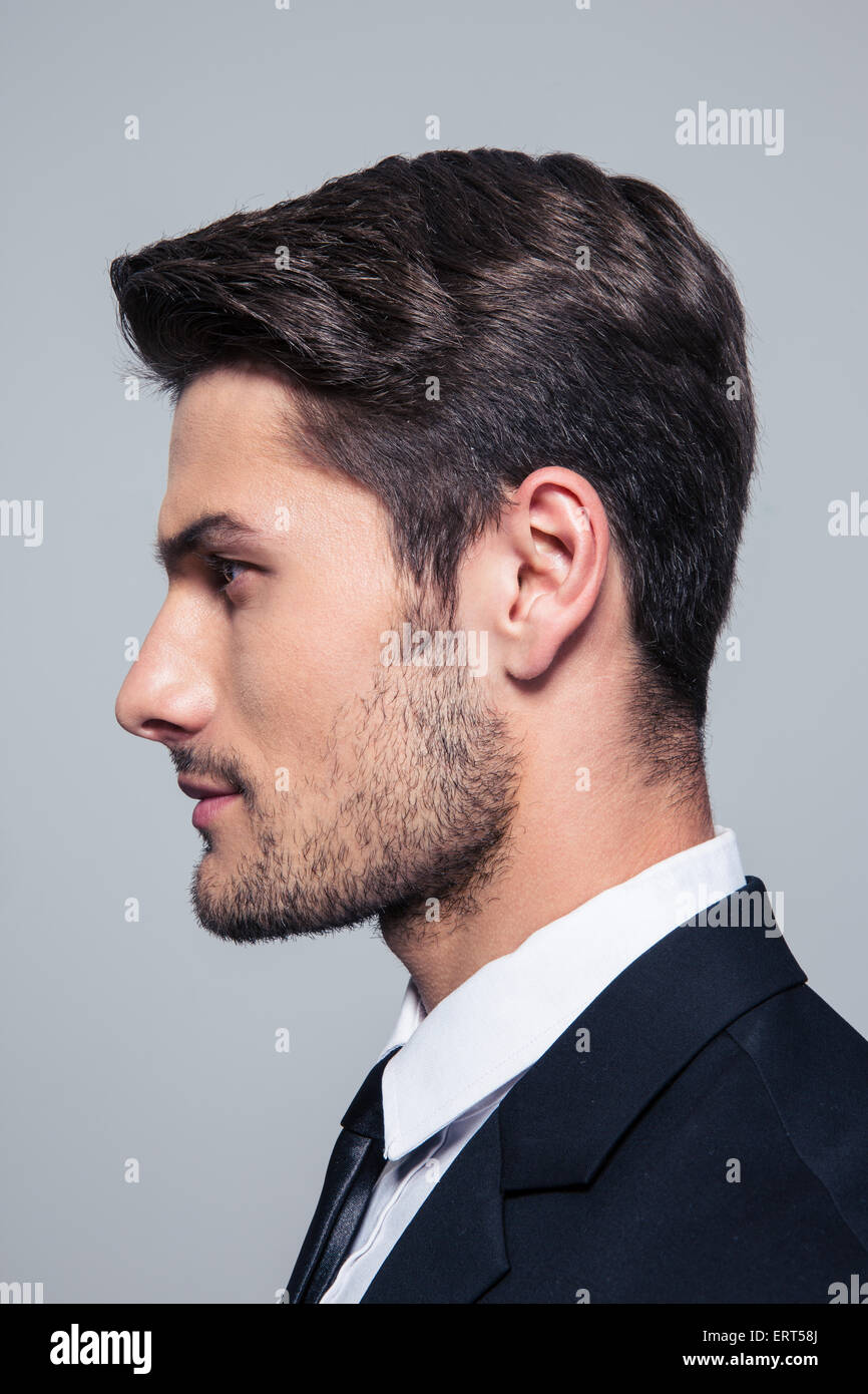 Vista lateral de un guapo empresario retrato sobre fondo gris Foto de stock