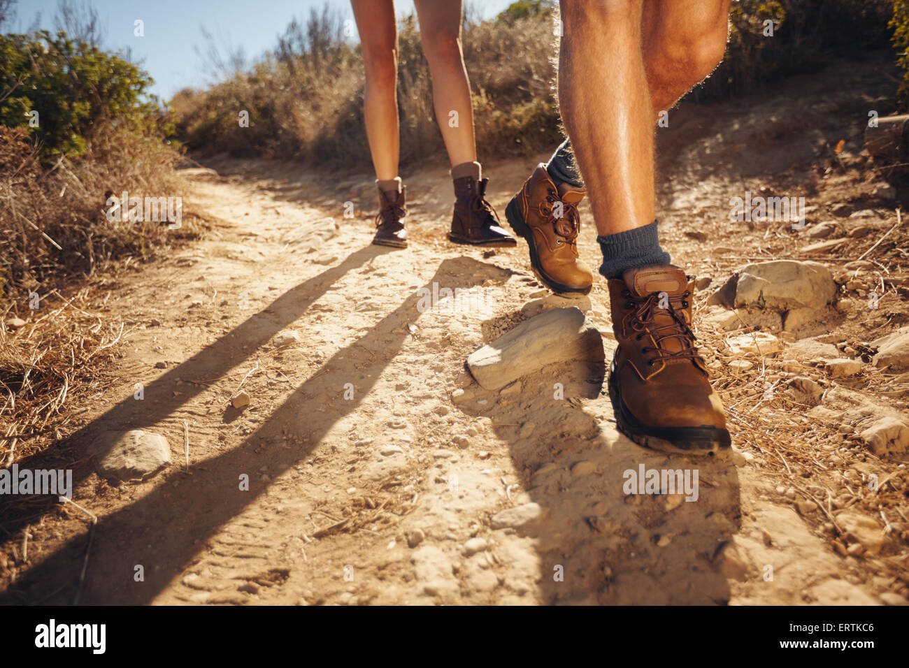 Cerca de las piernas de los jóvenes excursionistas caminando en la ruta del país. Pareja joven trail despertarse. Centrarse en el calzado de senderismo. Foto de stock