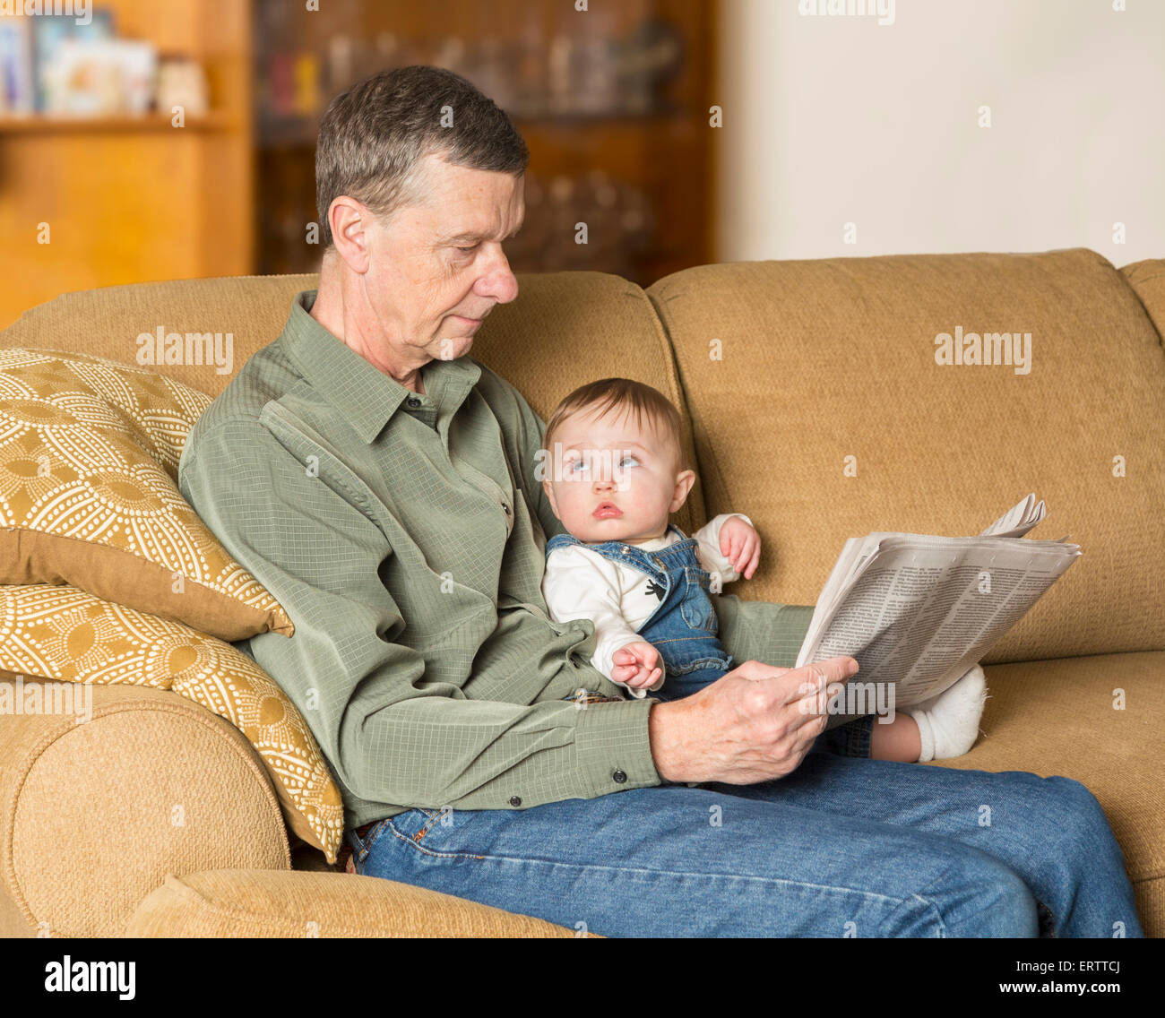 Baby Girl y abuelo leyendo el periódico en el sofá en el salón familiar Foto de stock