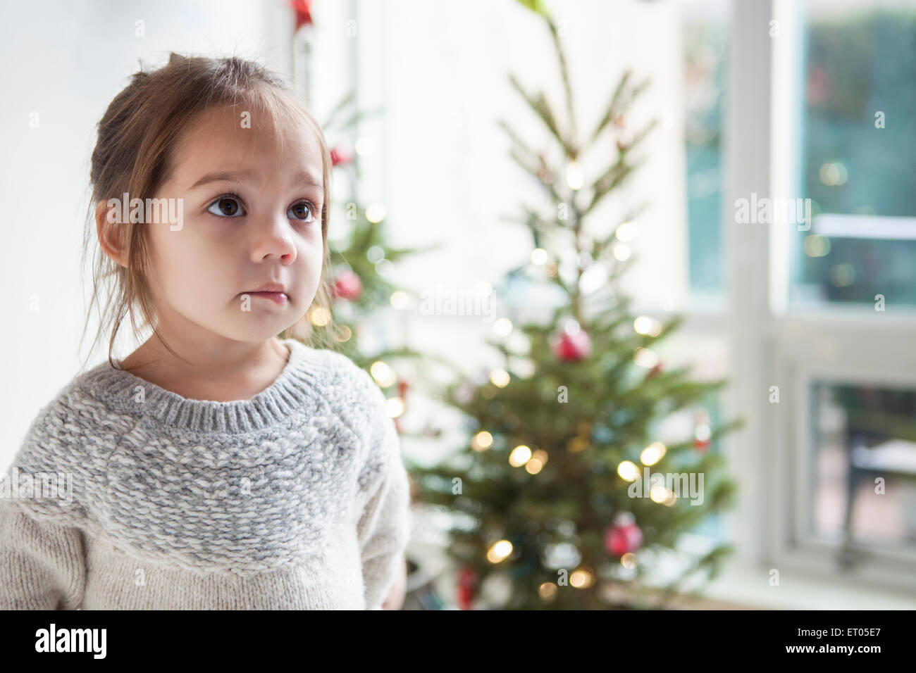 Wide-eyed girl mirando hacia arriba en la parte delantera del árbol de Navidad Foto de stock