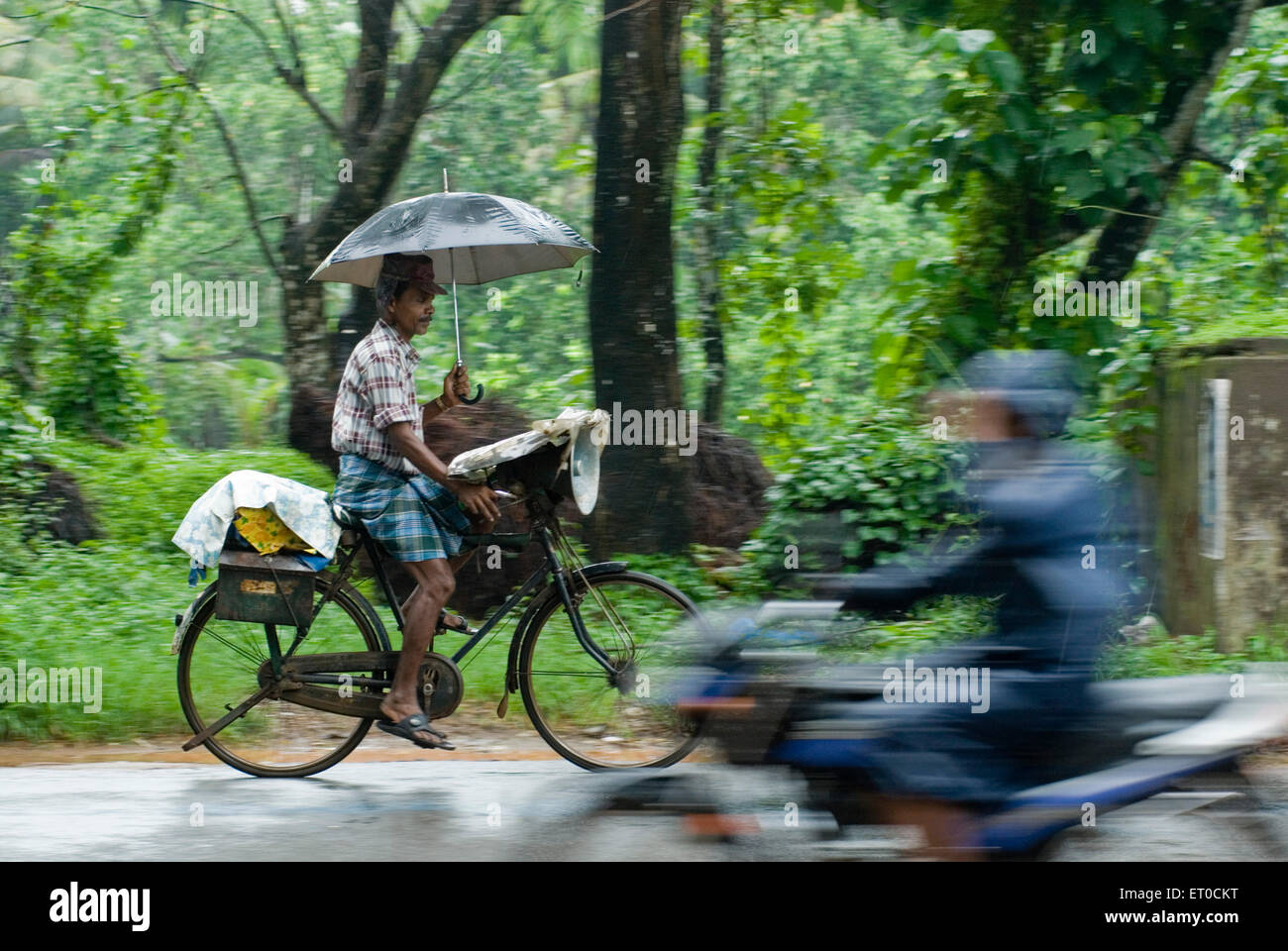 Billete de lotería vendedor montando bicicleta con paraguas en la lluvia ; ; Kerala India Foto de stock