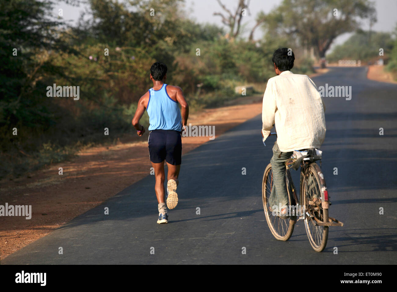 Atleta corriendo en carretera, seguidos por el ciclista en Bhopal, Madhya Pradesh, India ; Foto de stock