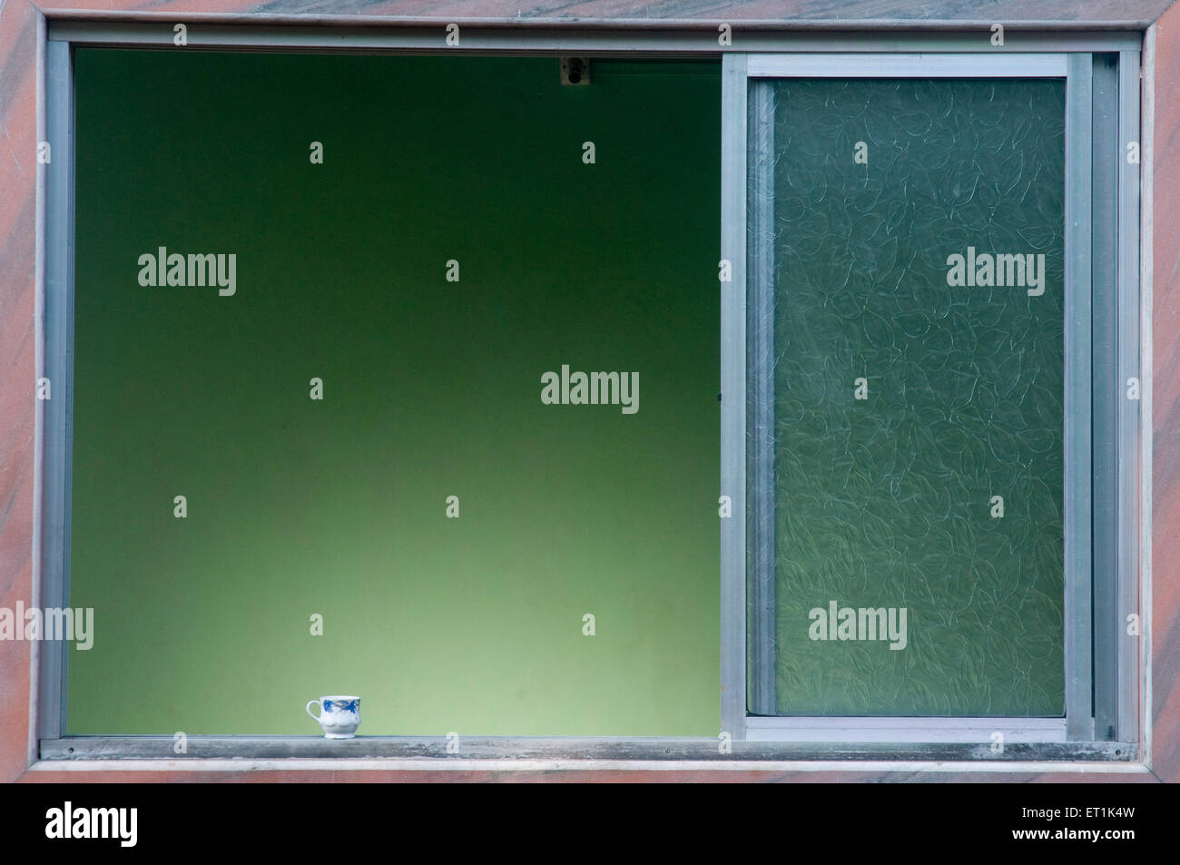 ventana de aluminio y copa de cerámica en el estante de borde del umbral de la ventana Foto de stock