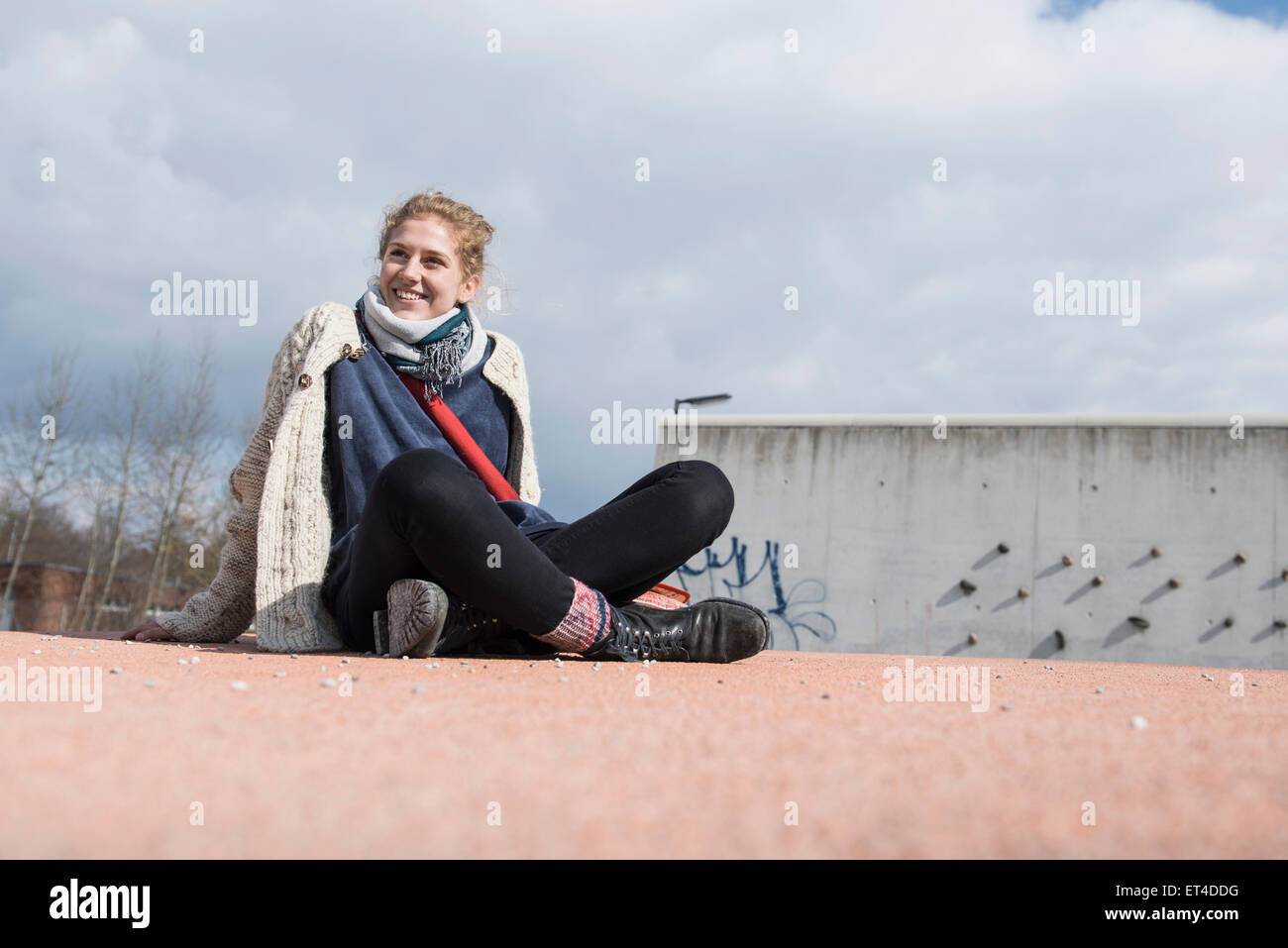 Mujer joven sentado con las piernas cruzadas en el campo de juegos de tocadiscos y sonriente Baviera Munich Alemania Foto de stock