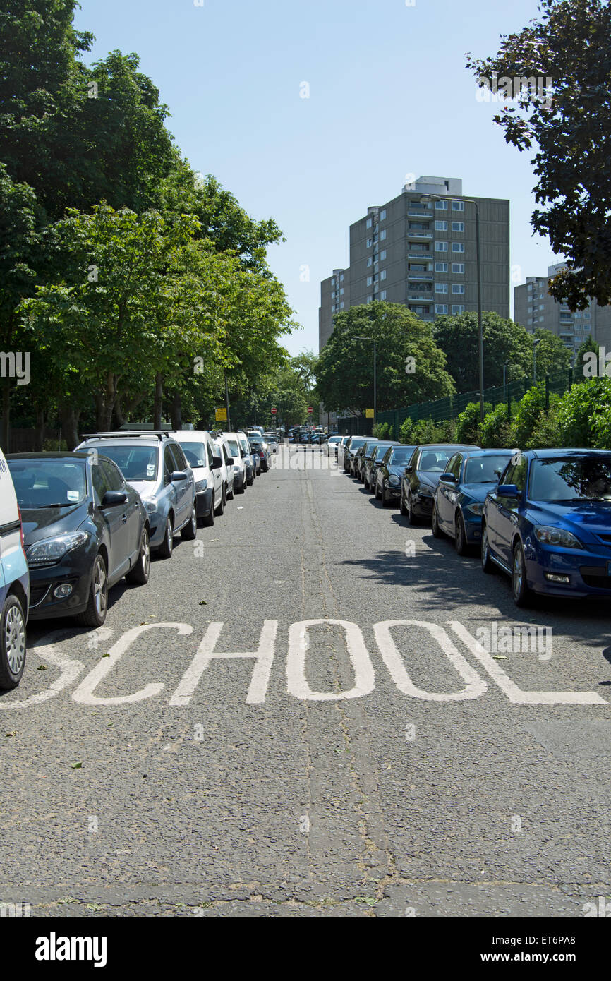 Señalización de carreteras para la escuela bordeado por a los paragolpes de autos estacionados Foto de stock