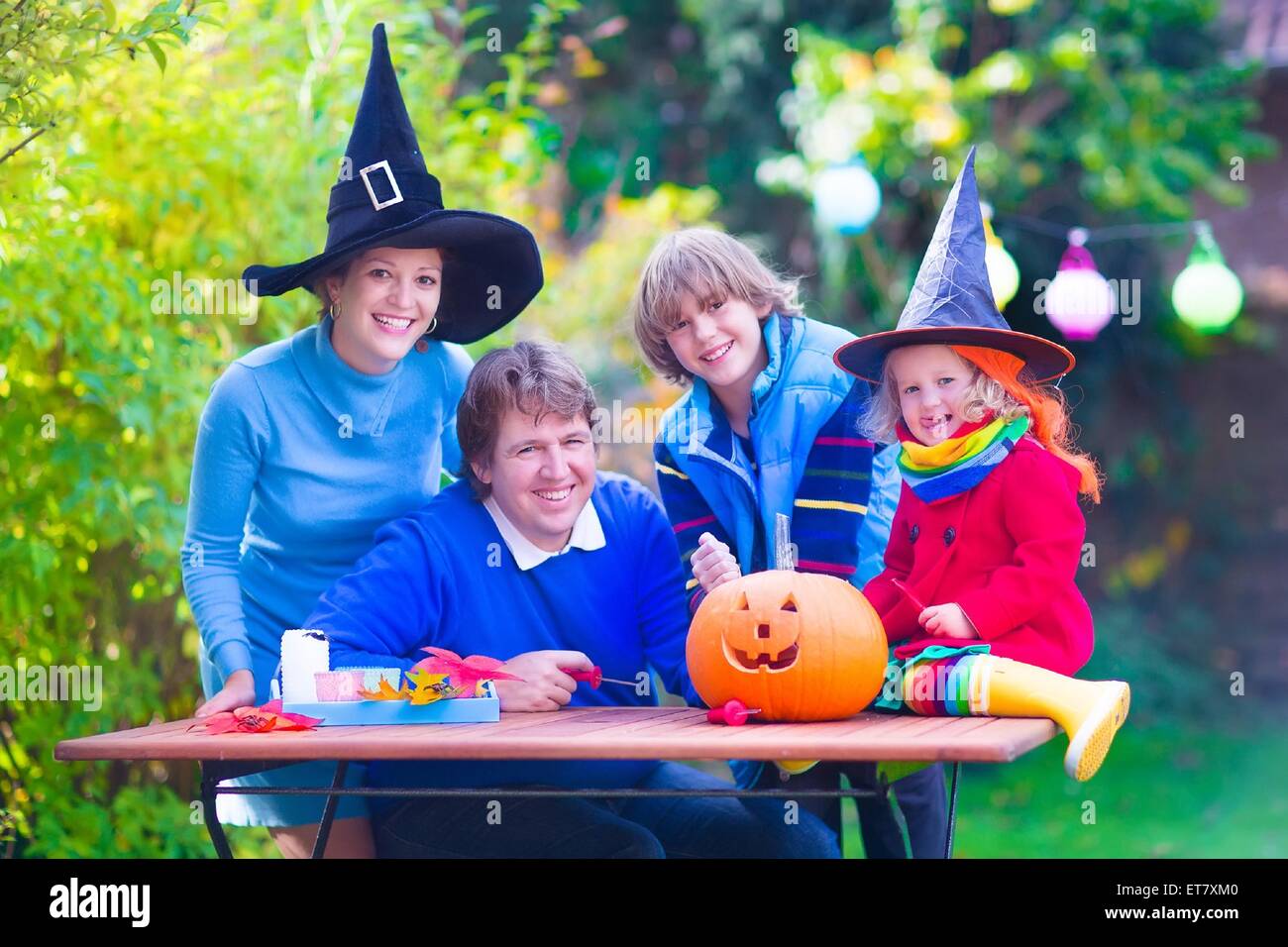 Familia Feliz, los padres con dos niños vestidos de traje y sombrero de bruja la celebración de Halloween y calabaza tallado en el jardín Foto de stock