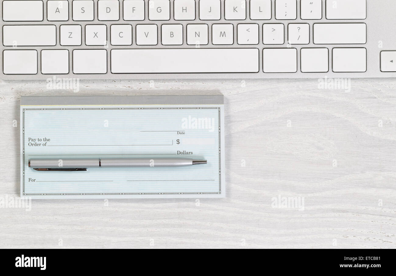 Imagen del teclado parcial con cheque en blanco y plata pluma sobre el escritorio blanco. Diseño en formato horizontal. Foto de stock