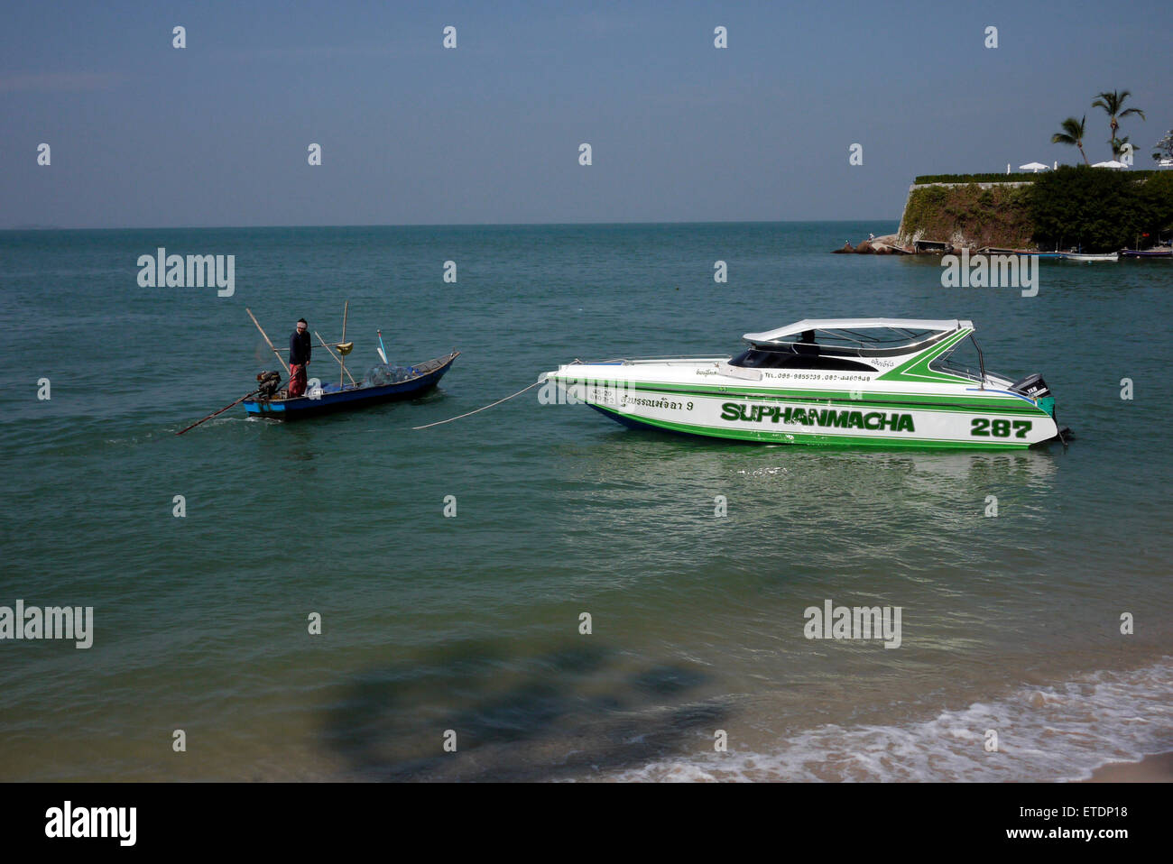 Con una sola mano pescador tailandés en su pequeño barco pesquero junto a una moderna lancha Foto de stock
