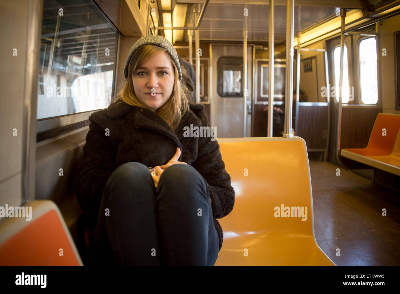 Mujer joven llevando un gorro calentito y untar sentado dentro de un tren subterráneo, cerca de Nueva York, Nueva York, EE.UU. Foto de stock
