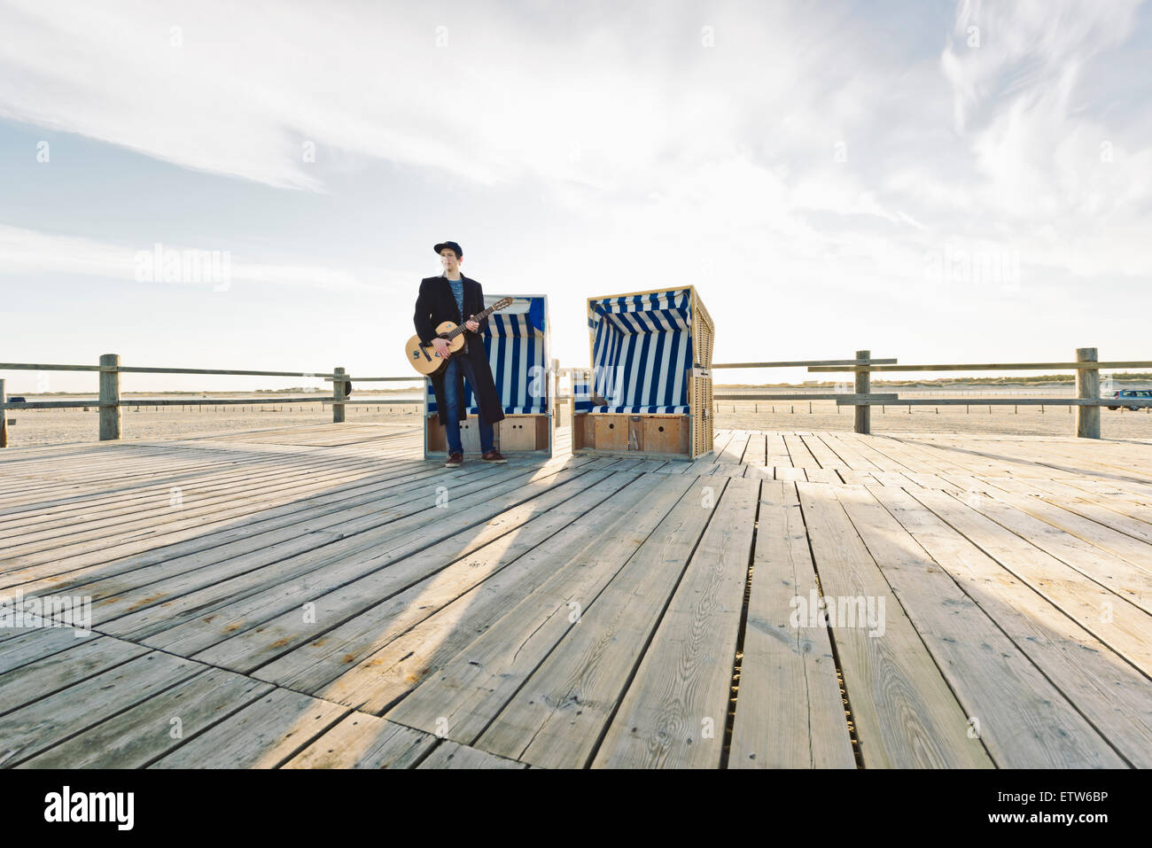 Alemania, Sankt Peter-Ording, adolescente con la guitarra de pie en frente de encapuchados, silla de playa Foto de stock