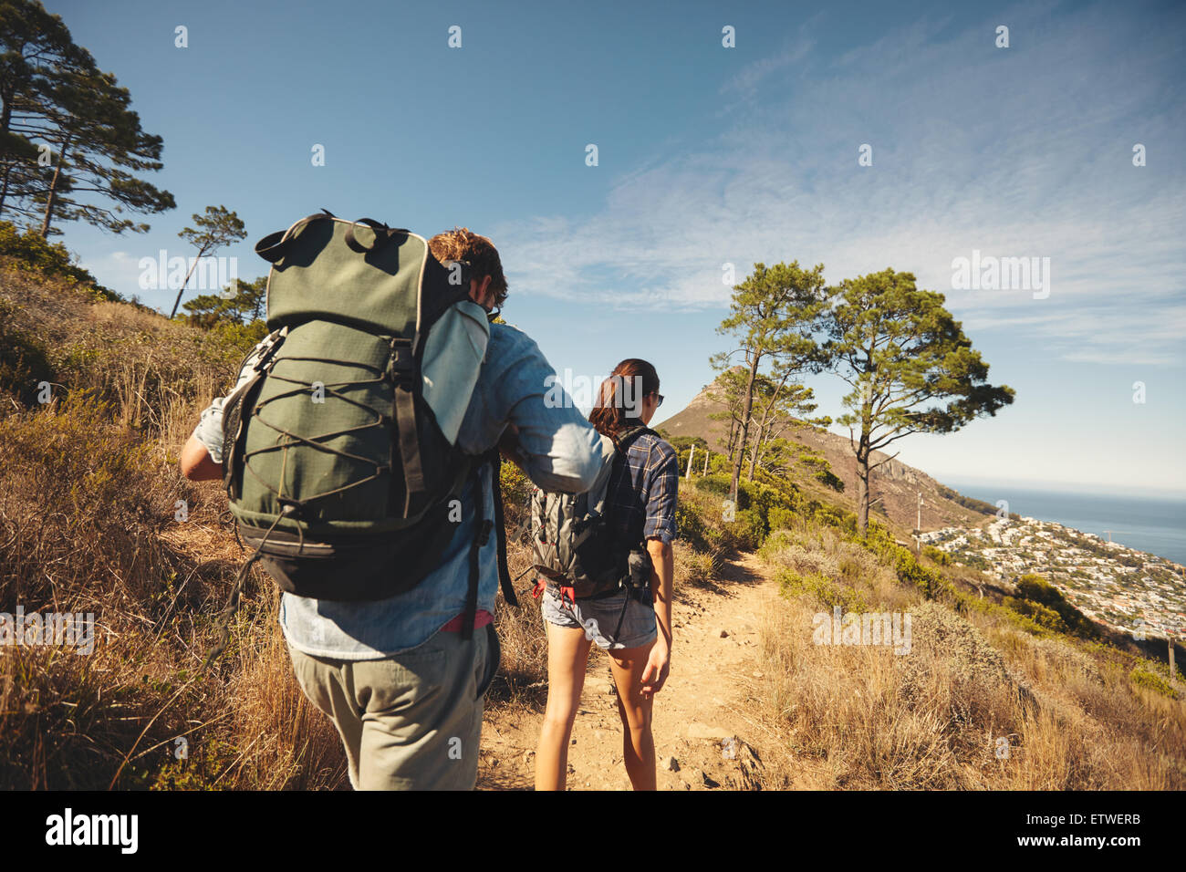 Vista trasera de dos jóvenes caminando por el sendero trazado en la montaña. Pareja joven caminatas con mochilas. Foto de stock