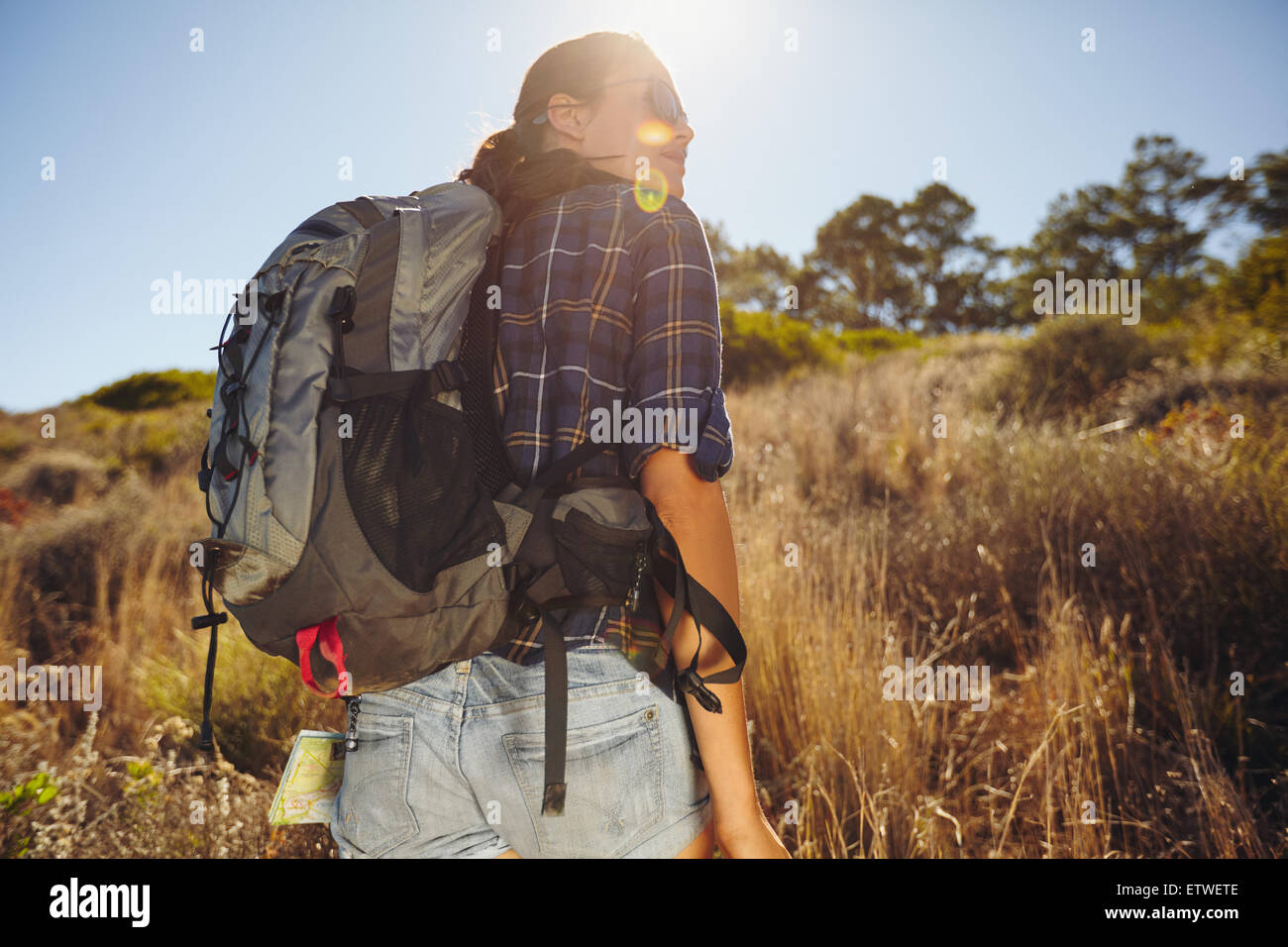 Vista trasera foto de joven mujer senderismo en verano. Mujeres caucásicas caminante en la montaña en busca de distancia en una vista con llamarada solar. Foto de stock