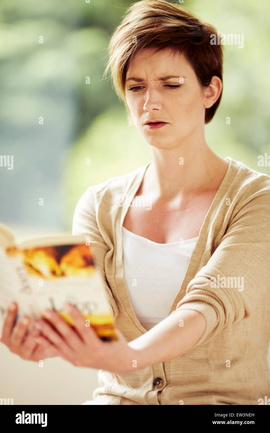 Mujer con mala vista luchando para leer libro Foto de stock