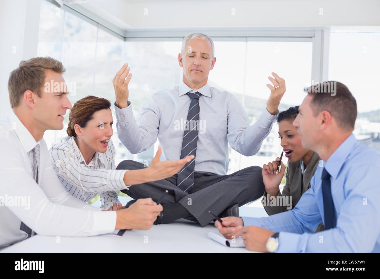 Empresario relajante sobre el escritorio con malestar colegas alrededor Foto de stock