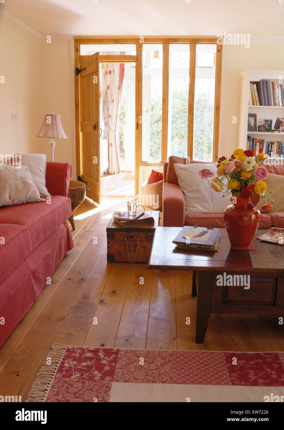 Suelos de madera y sofás de color rosa en la sala de estar con puertas de pino en el suelo hasta el techo, ventanas interiores Foto de stock