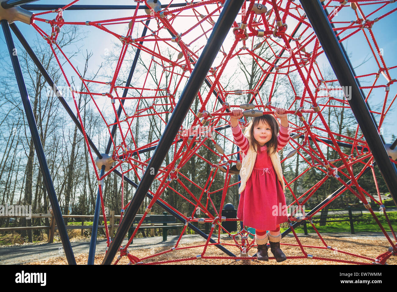 Chica jugando en un marco de escalada rojo en un parque, EE.UU Foto de stock