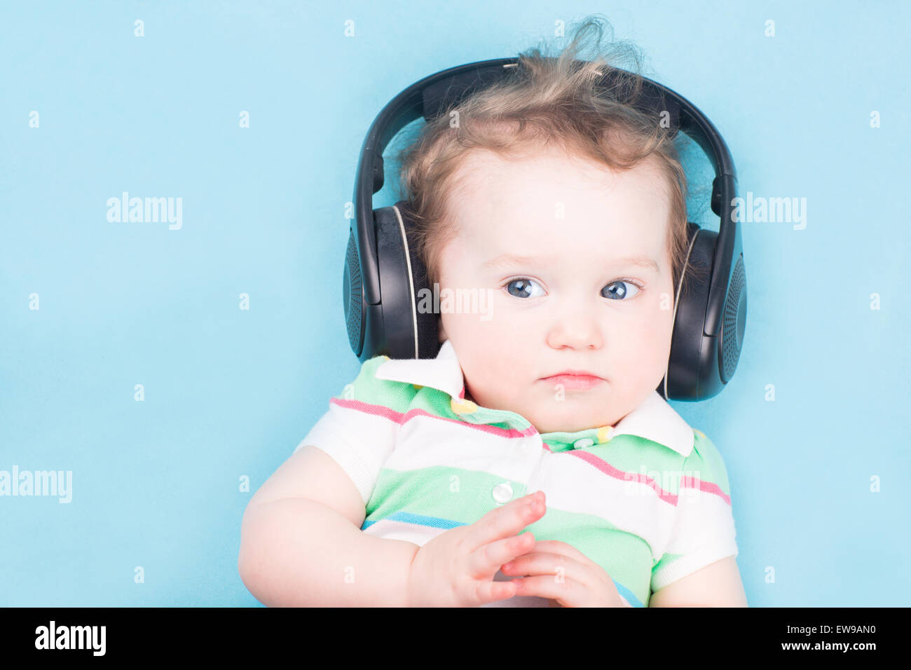 Bebé con auriculares escuchando música en una cama blanca en casa