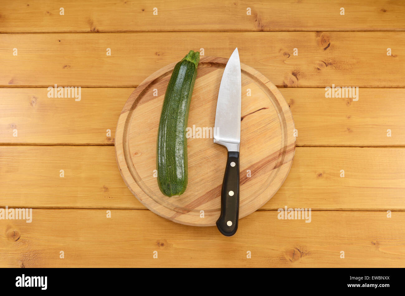 Todo el calabacín verde con un afilado cuchillo de cocina sobre una tabla de cortar de madera Foto de stock